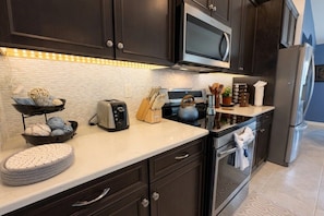 Uma cozinha moderna com armários escuros, micro-ondas, torradeira e chaleira na bancada.