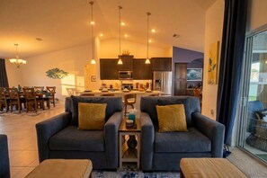 Uma sala de estar moderna com sofá, área de jantar com cadeiras e cozinha equipada.