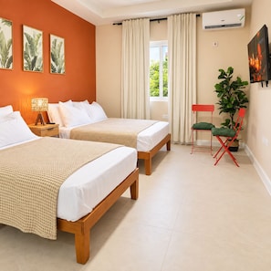 A hotel room with two beds, a nightstand, a lamp, a potted plant, a chair, and a TV. - Selah Oasis - Kingston 2BR, 3 Beds, Sleeps 5 ~ Pool, Parking & Central Location (Kingston)