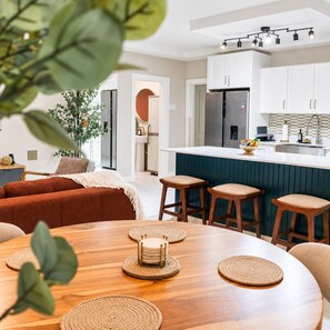 A modern kitchen with white cabinets, a central island, and bar stools. - Selah Oasis - Kingston 2BR, 3 Beds, Sleeps 5 ~ Pool, Parking & Central Location (Kingston)