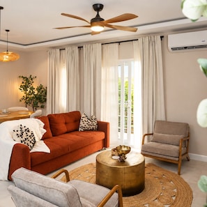 A living room with a sofa, armchair, and round coffee table, a ceiling fan, and a view through large windows. - Selah Oasis - Kingston 2BR, 3 Beds, Sleeps 5 ~ Pool, Parking & Central Location (Kingston)