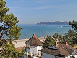 A coastal building with a beach in the background, a pier extending into the water, and a mountainous landscape. - No. 9 in Villa Aegir (Binz)