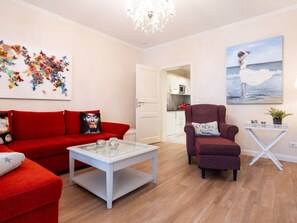 A living room with a red sofa, a glass coffee table, a red armchair, a painting of a woman by the sea, and a colorful butterfly wall art. - No. 9 in Villa Aegir (Binz)