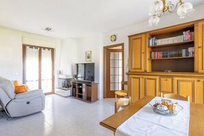 Una sala de estar con un sofá, una mesa de comedor con una cesta de fruta, un televisor y una estantería.