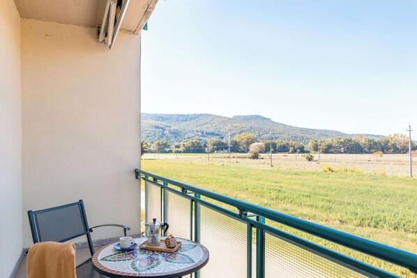 Un balcón con mesa, silla y vistas a un campo verde y colinas.