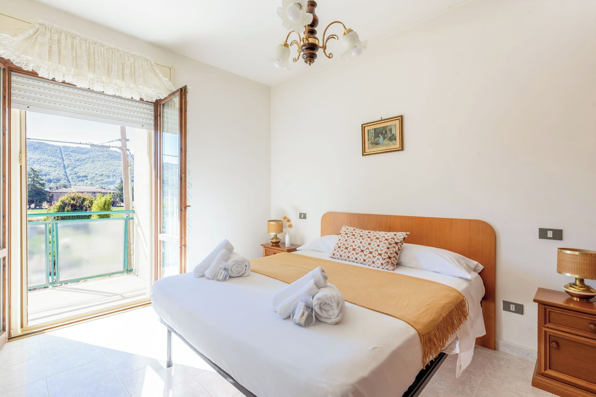 Una habitación de hotel con una cama, una mesita de noche, una lámpara, un cuadro en la pared y vista a una montaña a través de la ventana.