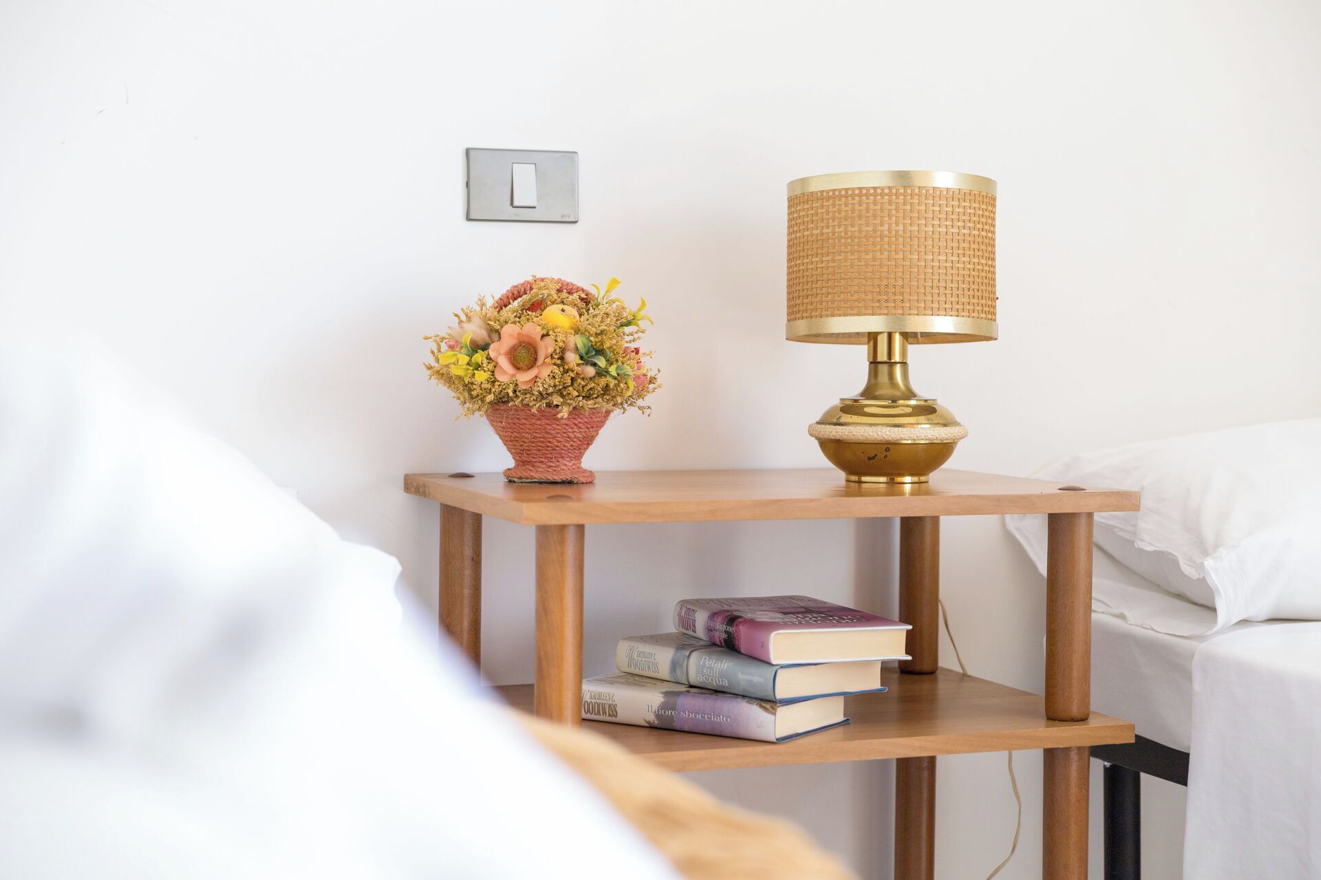 Une table de chevet avec une lampe, un vase de fleurs et des livres.
