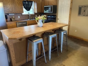 A kitchen with wooden cabinets, a stainless steel sink, a microwave, and a stove. There are two metal stools and a vase with flowers on the counter. - Serene 3-bedroom house in charming Lone Grove (Lone Grove)