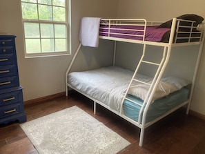 Ein Etagenbett mit weißer Matratze und einer violetten Decke, einem weißen Kissen und einer blauen Schubladenkommode.