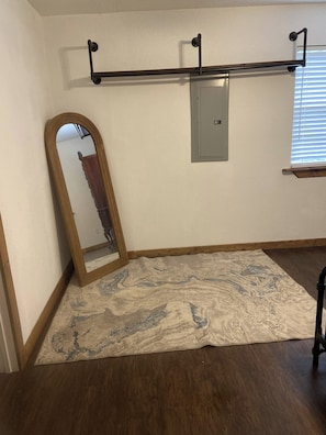 Ein Zimmer mit Holzboden, einem Teppich mit Marmoroptik, einem Spiegel in voller Größe, einem Metallheizkörper und einem Fenster mit Jalousien.
