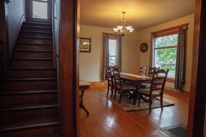A dining room with a wooden table, chairs, a chandelier, and a staircase leading to another level.