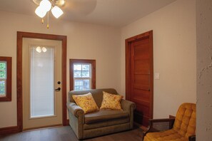 A room with a wooden door, a window with blinds, a sofa with floral cushions, and a chair. - Spacious house that sleeps 11 people. Perfect for families traveling together. (Colby)