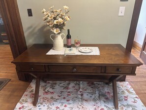 A wooden table with a vase of flowers, a bottle, and a plate on a floral table runner.
