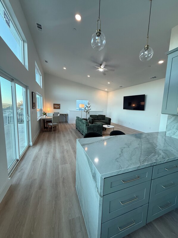 A spacious kitchen with a marble countertop, a dining area with a green sofa, and a television mounted on the wall.