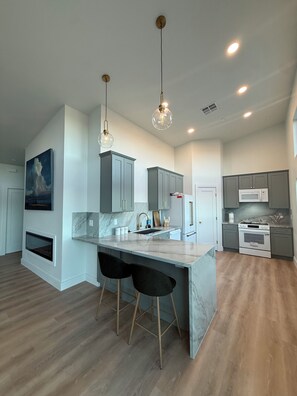 A modern kitchen with a marble countertop, two bar stools, pendant lighting, and a built-in oven. - New 2/1 Home in Kelly Ridge with beautiful views (Oroville)