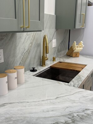 A kitchen with a marble countertop, a gold faucet, and wooden cabinets.