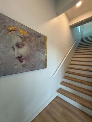 A staircase with wooden steps and a white handrail, leading to a landing where a large abstract painting is displayed on the wall. - New 2/1 Home in Kelly Ridge with beautiful views (Oroville)