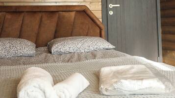 Ein Schlafzimmer einer Holzhütte mit schrägem Dach, einer dunklen Tür und einem Bett mit einem gemusterten Bettbezug und Kissen.