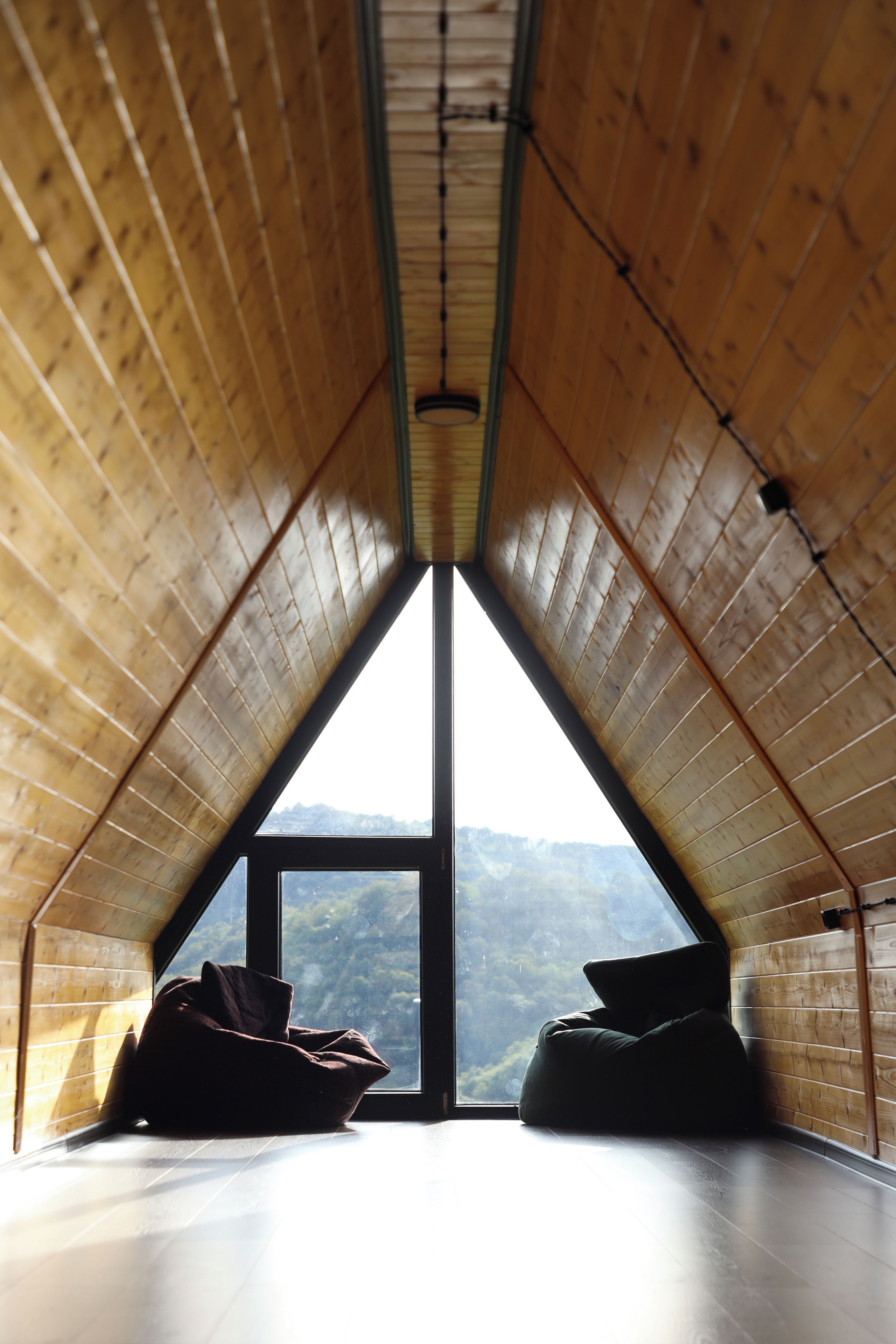 An attic room with a sloped ceiling, a large window, and two bean bags.
