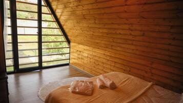 A room with a sloped ceiling, wooden walls, a bed with a white bedspread, and a window with a view of greenery.