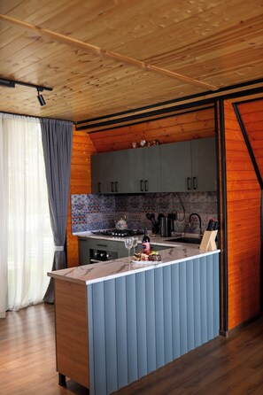 A modern kitchen with wooden cabinetry, a marble countertop, and a built-in island with bar stools. - Lovely 4-bedroom cottage in superb Kutaisi location perfect for families (Kutaisi)