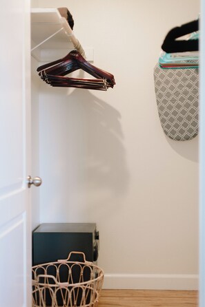 Un placard rempli de vêtements suspendus, un sac à motifs et un panier en osier.