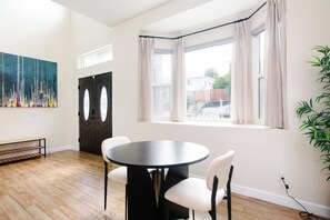 A room with a round black table, white chairs, a bench, a large abstract painting, a dark door, a window with curtains, and a plant. - California dreamin hilltop views! 4 bedrooms & 3 full baths (Los Angeles)