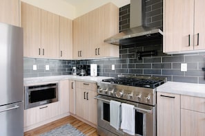 Une cuisine moderne avec des meubles de couleur bois clair, un réfrigérateur en acier inoxydable, un four encastré, une cuisinière à gaz et un dosseret de crédence en carreaux noirs.