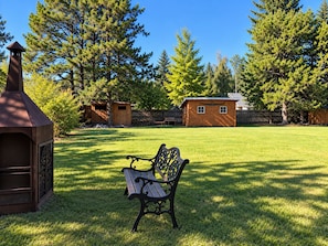 En trädgård med en träbänk, en grill och ett litet trähus.