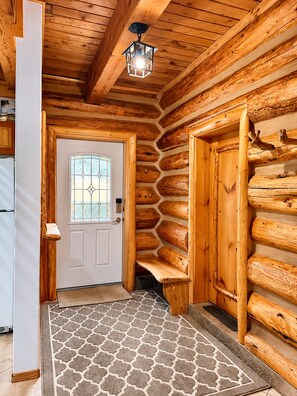 A log cabin interior with a wooden door, a staircase, and a patterned rug. - Cranberry Mountain Lodge - Valemount (Valemount)