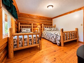 Ein Blockhaus-Zimmer mit zwei Holzbetten, einem Fenster mit Vorhängen und einer Deckenleuchte.