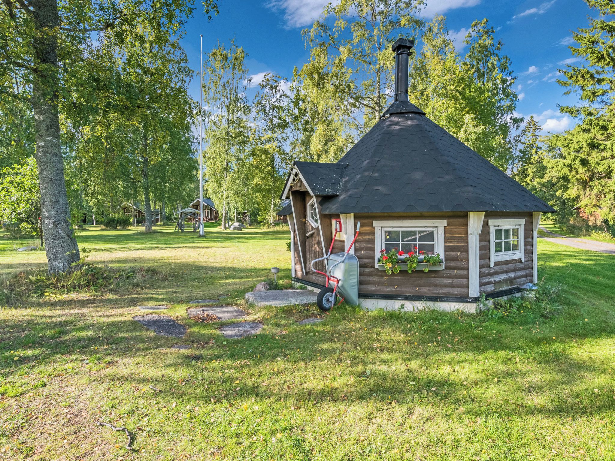 A small wooden cabin with a black roof, surrounded by a grassy area with trees.