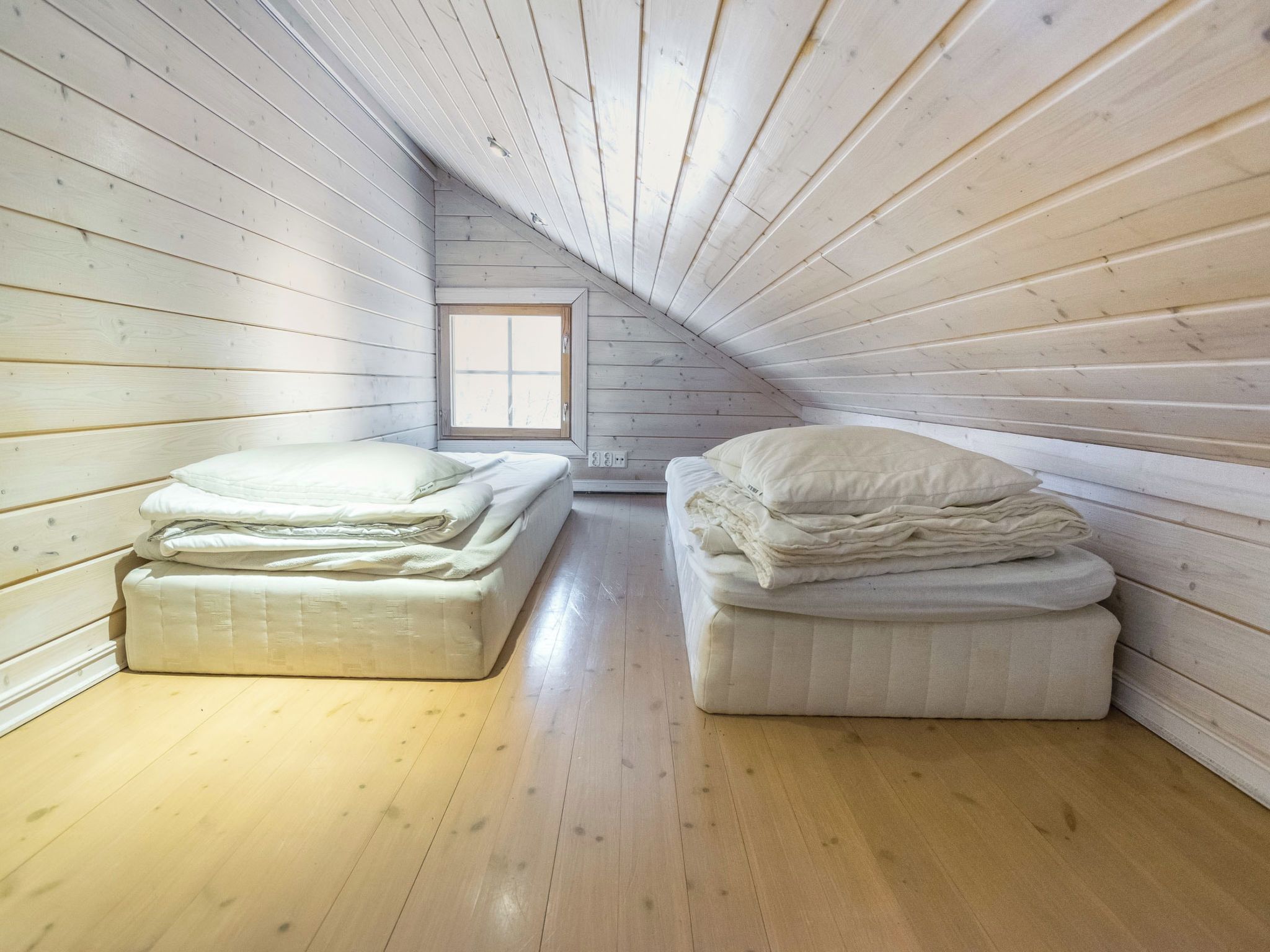 A small attic bedroom with wooden walls and a sloped ceiling. There are two beds with white bedding.