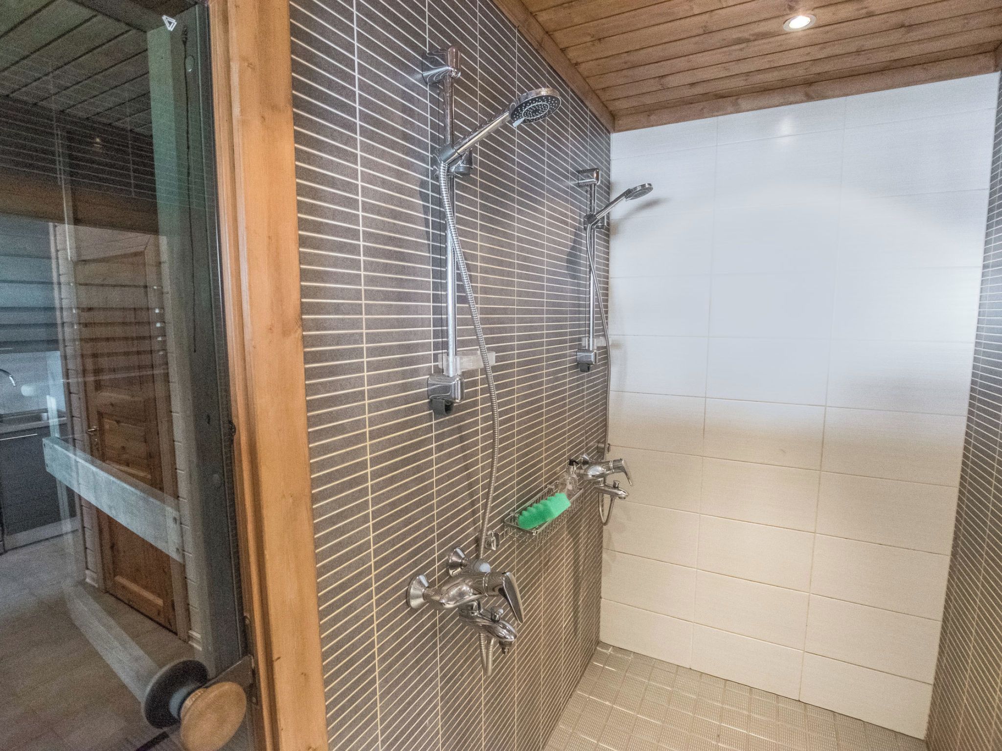 A shower area with multiple showerheads and a handheld shower attachment, a green sponge, and a towel rack.