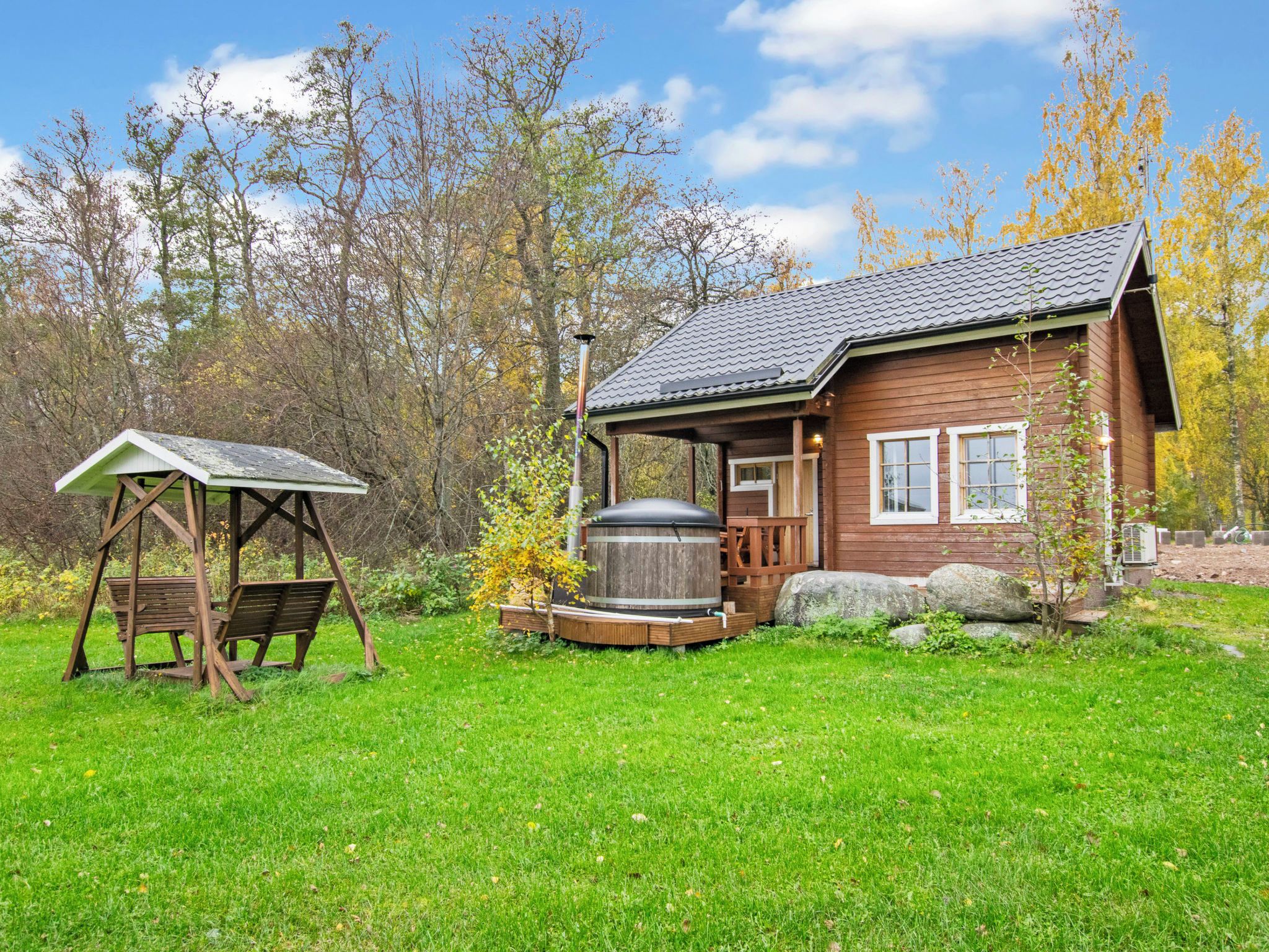 A wooden cabin with a porch, a swing set, and a large barrel.