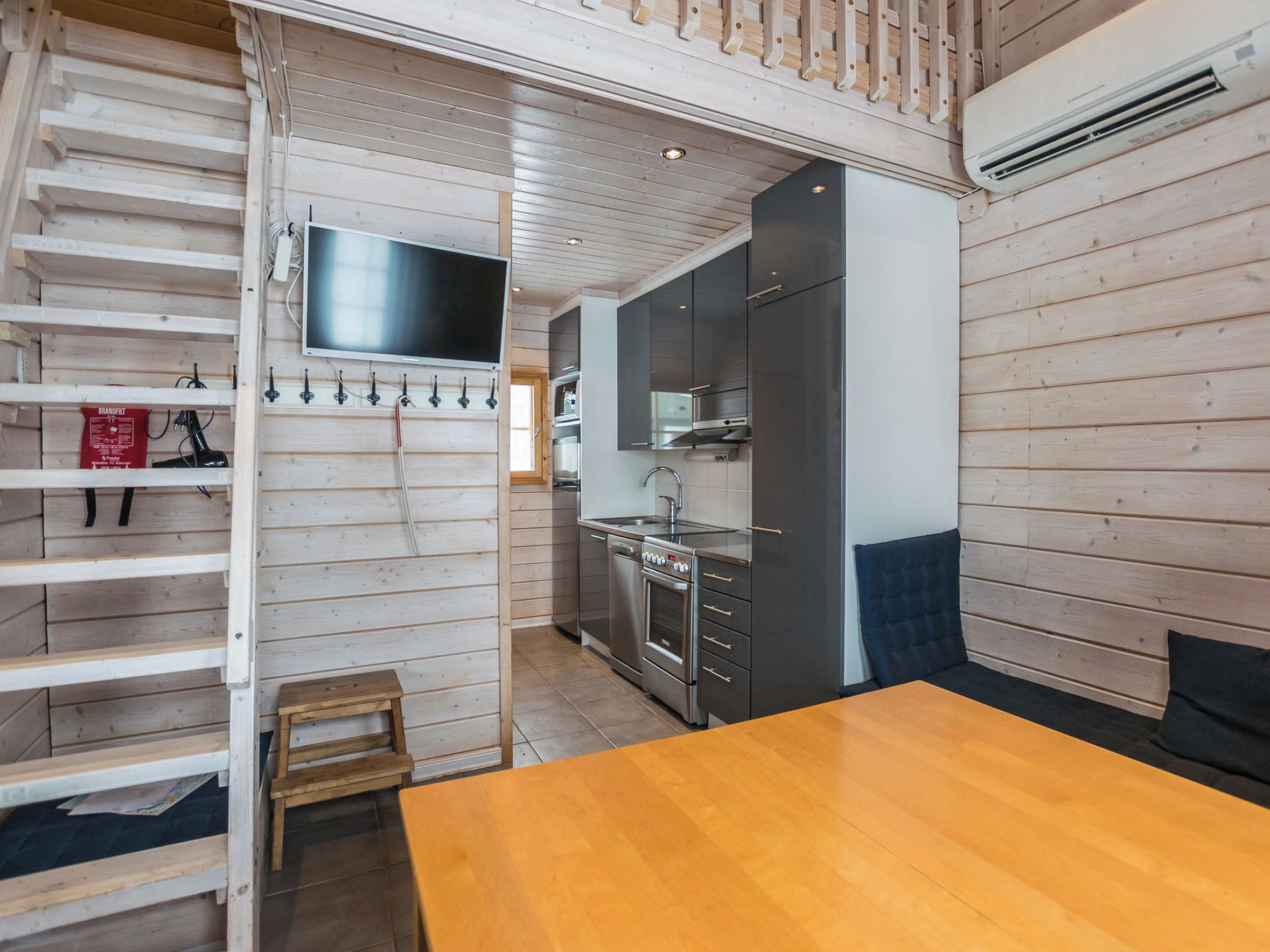 A compact kitchen with modern appliances, a wooden dining table, and a built-in TV.