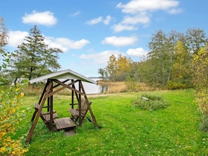 A wooden swing set with a bench in a grassy area with trees and a body of water in the background.