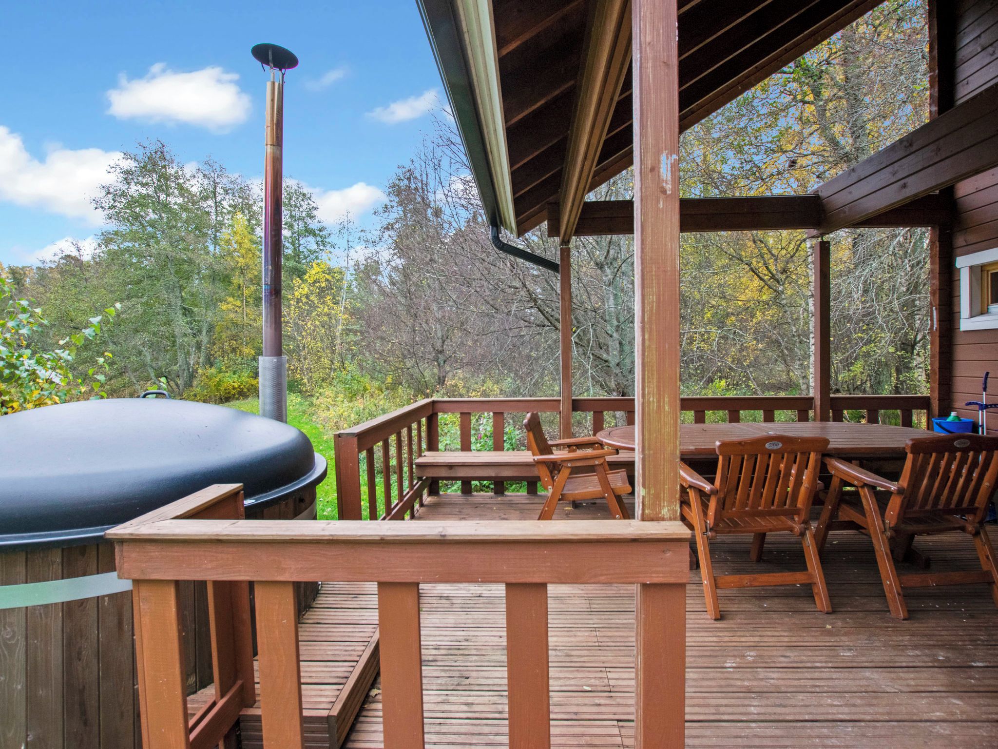 A wooden deck with a grill, chairs, and a table.