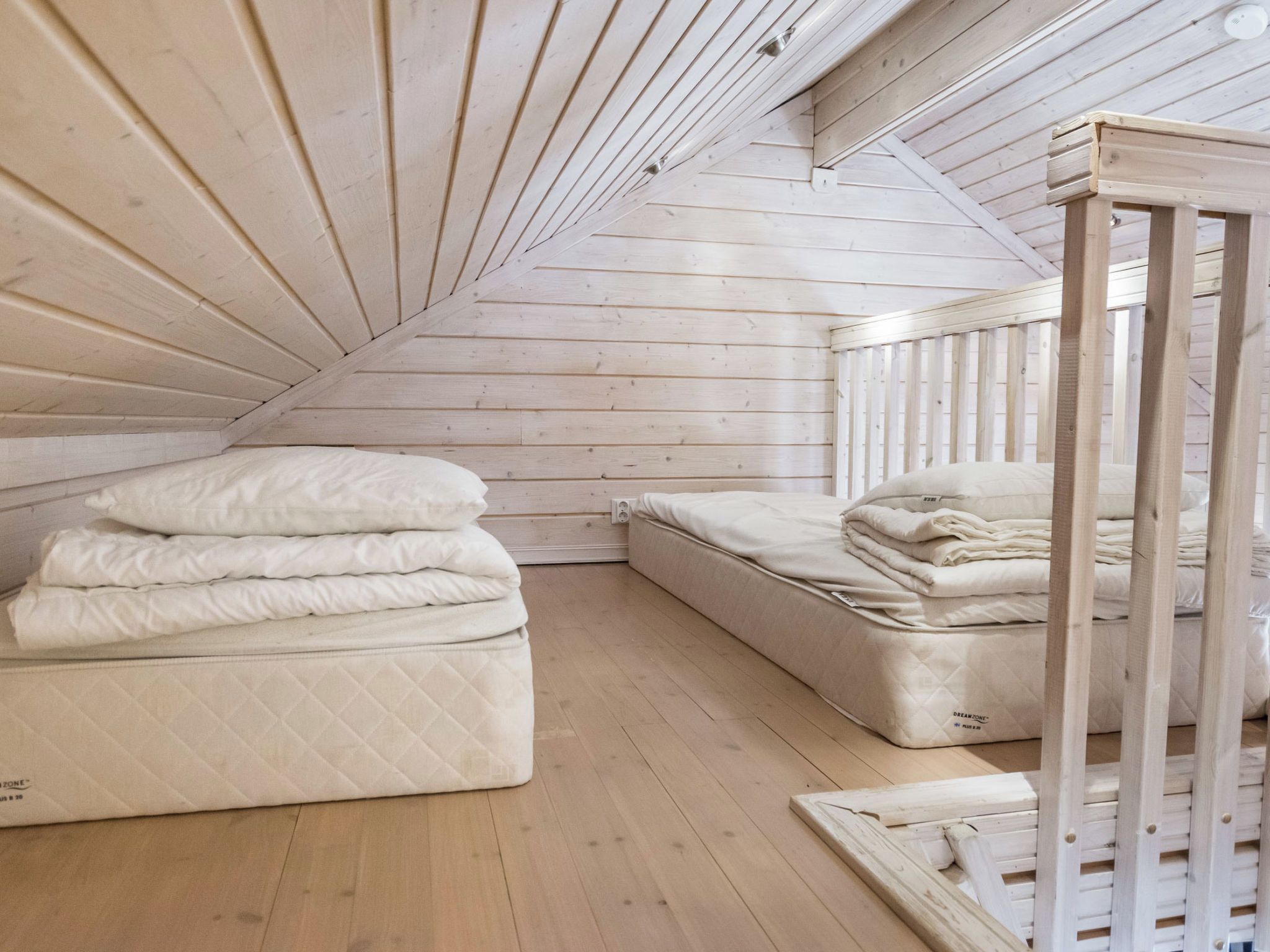 Een slaapkamer in een loft met een schuine kap, houten balken en twee matrassen.
