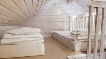 Een slaapkamer in een loft met een schuine kap, houten balken en twee matrassen.
