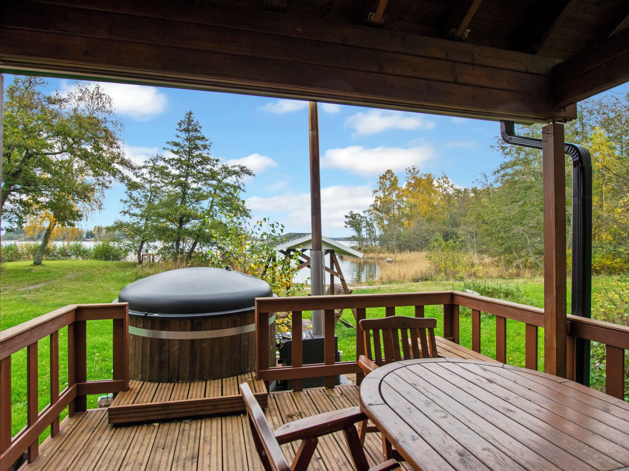 A wooden deck with a table and chairs, a hot tub, and a view of a lake and trees.