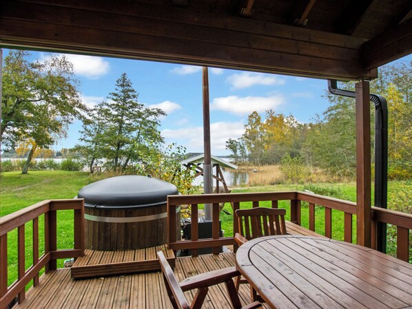 A wooden deck with a table and chairs, a hot tub, and a view of a lake and trees.