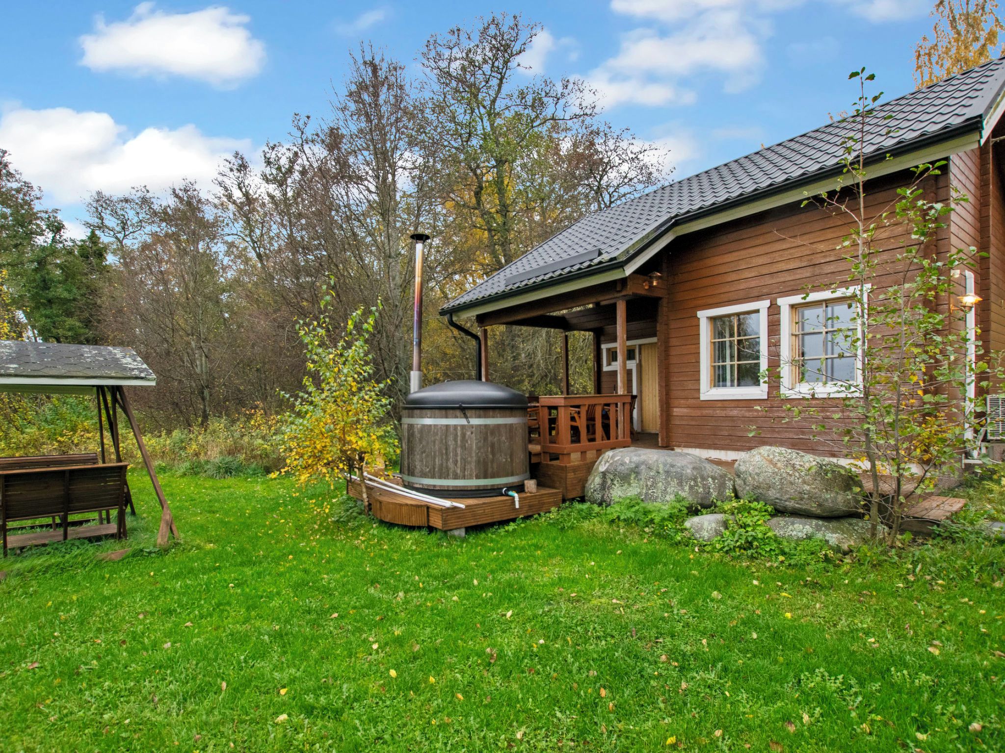 A wooden cabin with a porch, a large barrel, and a bench in a grassy yard.