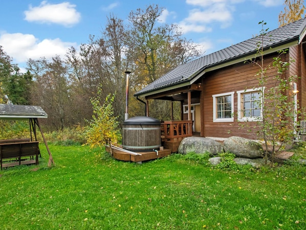 A wooden cabin with a porch, a large barrel, and a bench in a grassy yard.