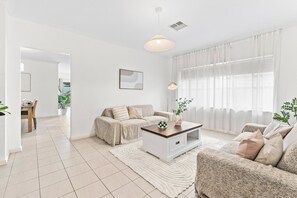 A modern living room with a sofa, a coffee table, and a dining area with a table and chairs. - Seednest | Spacious Magill BBQ Family Retreat (Magill)