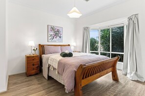 A bedroom with a wooden bed, bedside tables, a window with curtains, and a wall-mounted lamp. - Seednest | Spacious Magill BBQ Family Retreat (Magill)
