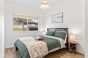 A bedroom with a bed, a window, a lamp, and a painting on the wall. - Seednest | Spacious Magill BBQ Family Retreat (Magill)
