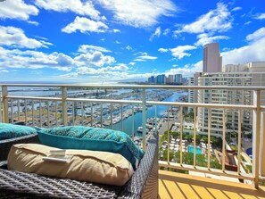 A balcony with wicker furniture and a view of a marina and buildings. - @ Marbella Lane - Dreamy OceanView | Lanai Waikiki (Honolulu)