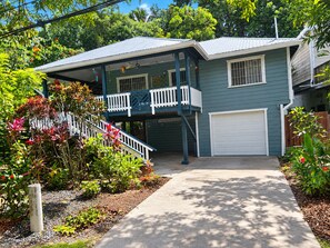 A two-story house with a covered porch, a garage, and a landscaped garden with various plants and flowers. - 3bed treat in West End with A/C, WiFi, parking. Chief's Haven (Roatan)