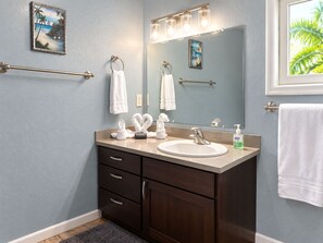 A bathroom with a vanity, a mirror, a towel rack, and a window with a view of palm trees. - 3bed treat in West End with A/C, WiFi, parking. Chief's Haven (Roatan)